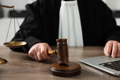 Judge with gavel and laptop sitting at wooden table indoors, closeup