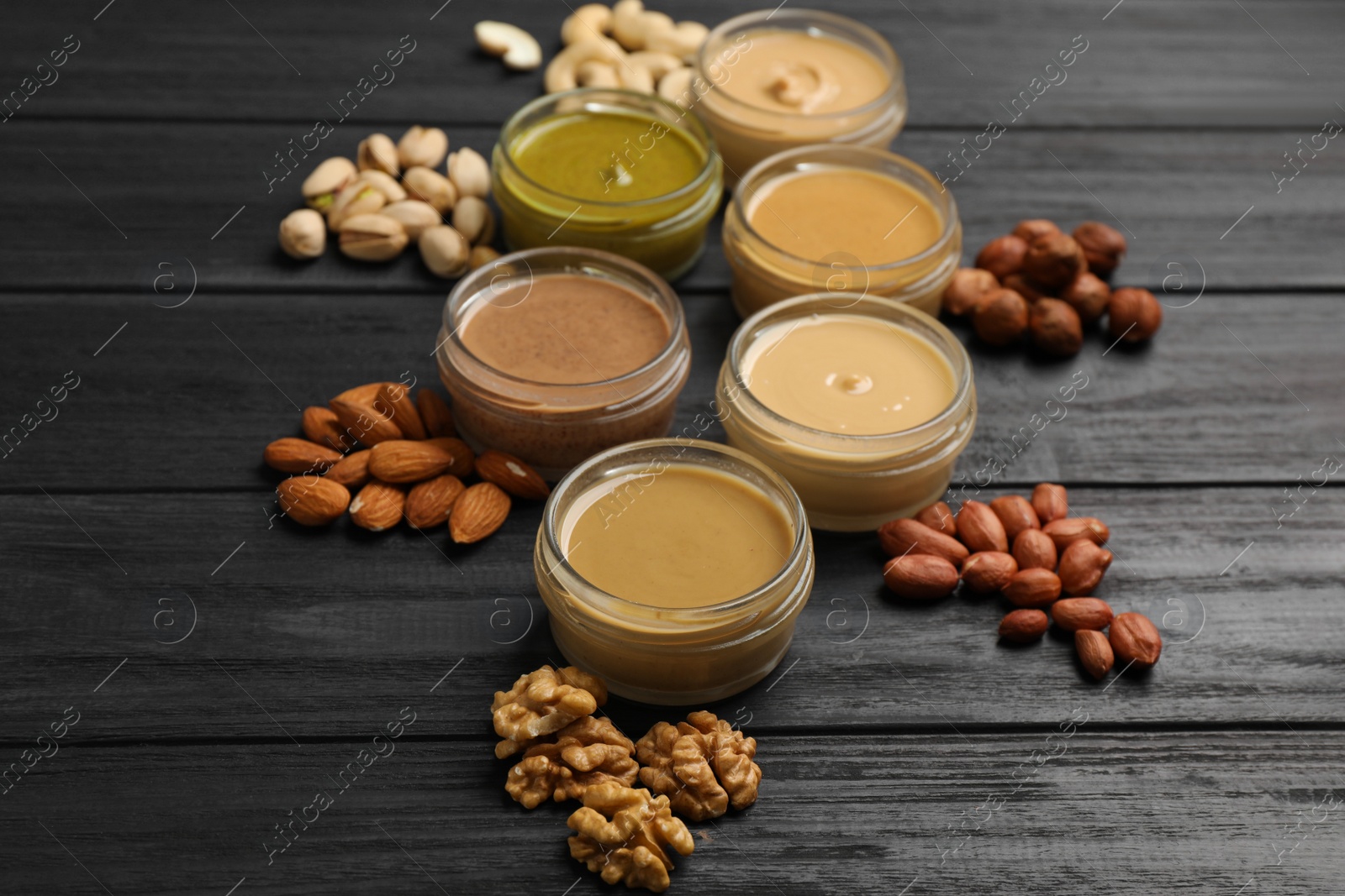 Photo of Jars with butters made of different nuts and ingredients on black wooden table