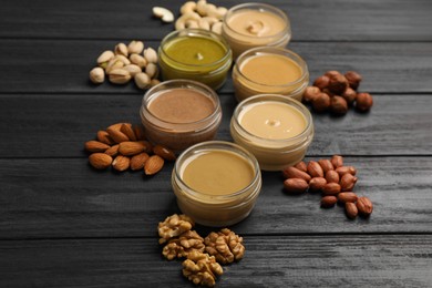 Photo of Jars with butters made of different nuts and ingredients on black wooden table