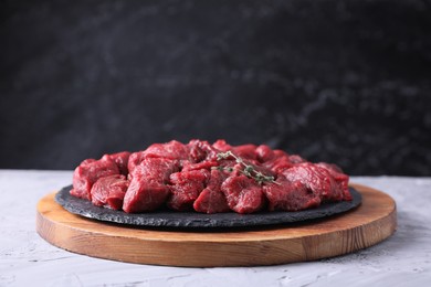 Photo of Pieces of raw beef meat and thyme sprigs on grey textured table against black background