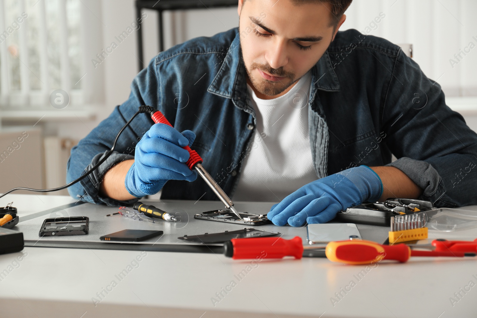 Photo of Technician repairing broken smartphone at table in workshop