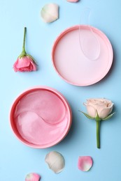 Under eye patches in jar and rose flowers on light blue background, flat lay. Cosmetic product
