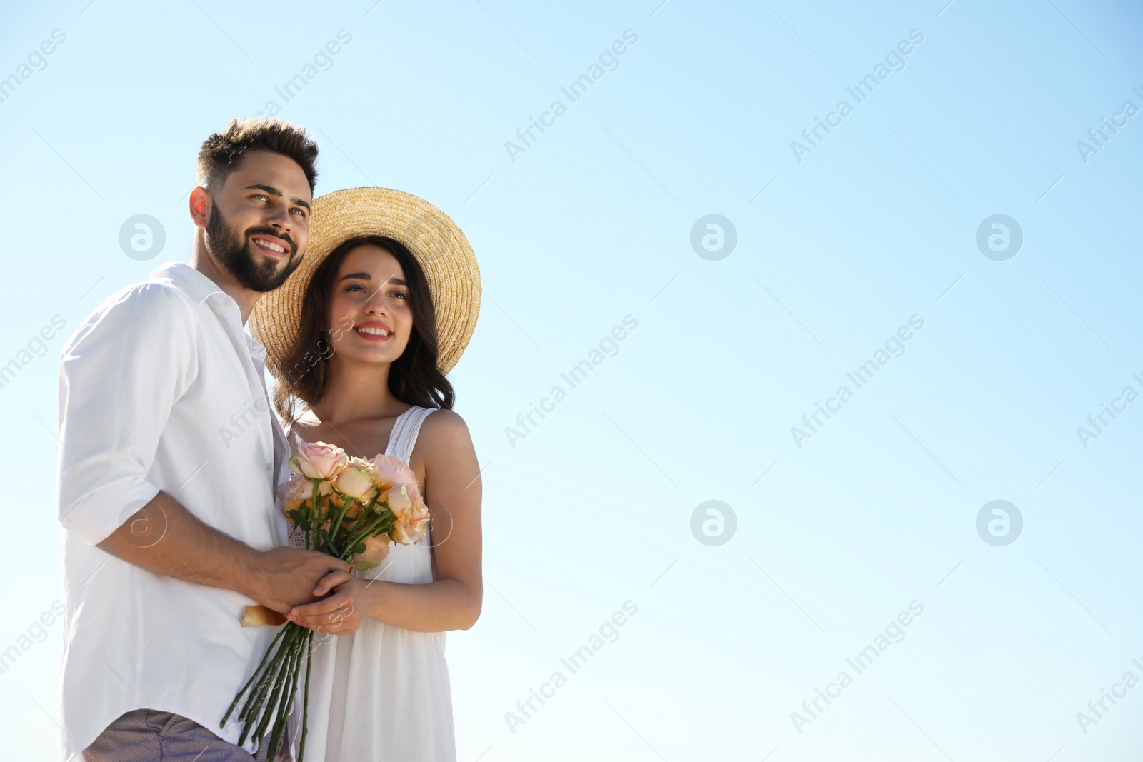 Photo of Happy young couple with flowers against blue sky. Honeymoon trip