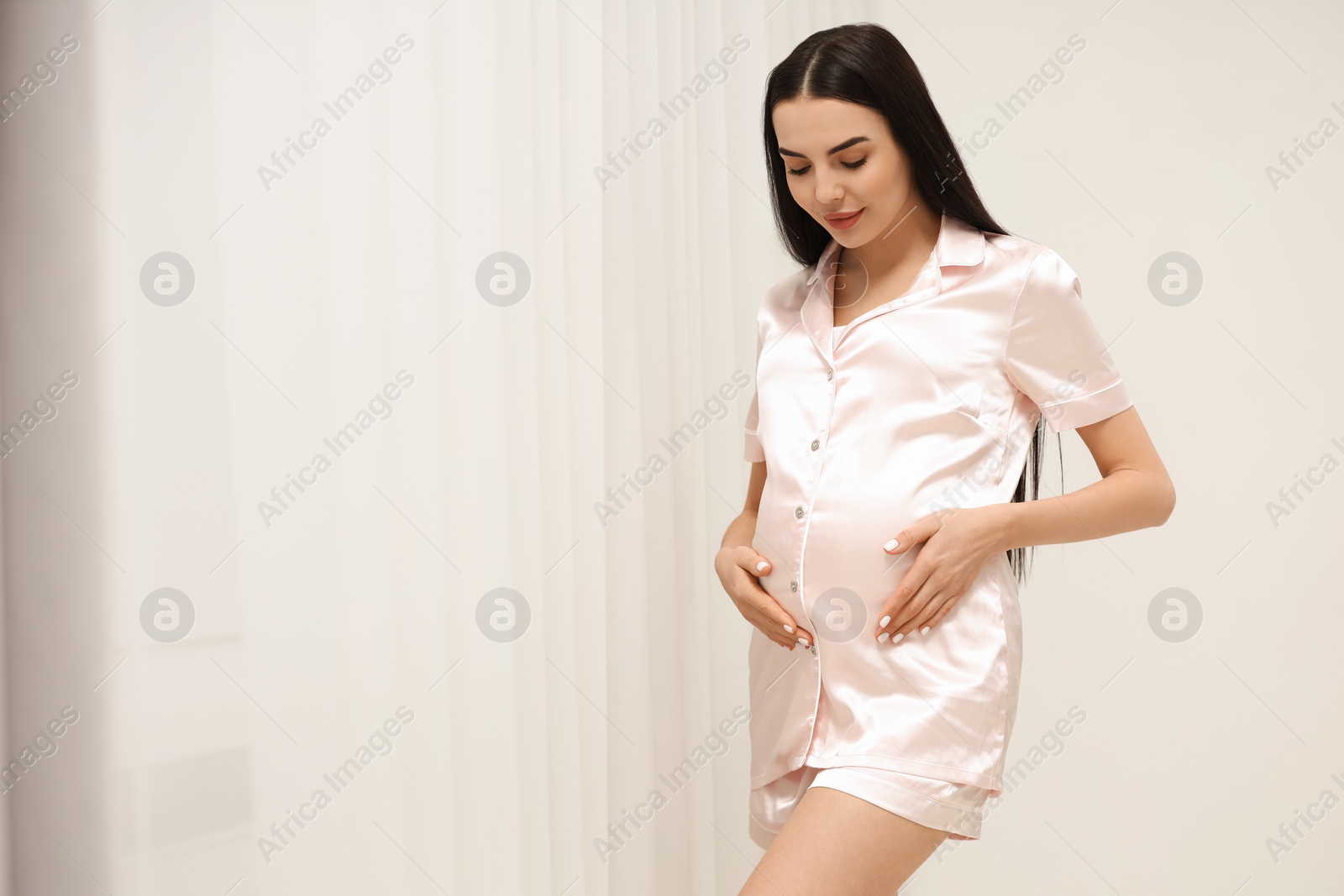 Photo of Pregnant young woman near window indoors, space for text