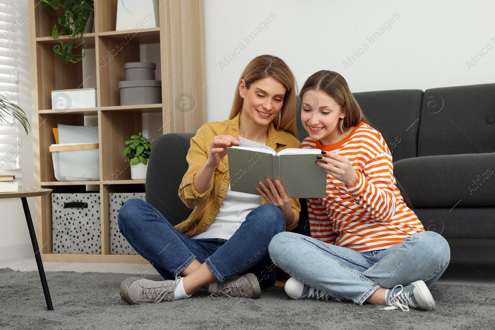 Photo of Happy mother and her teenage daughter reading book on floor at home