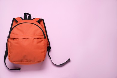 Stylish orange backpack on violet background, top view. Space for text