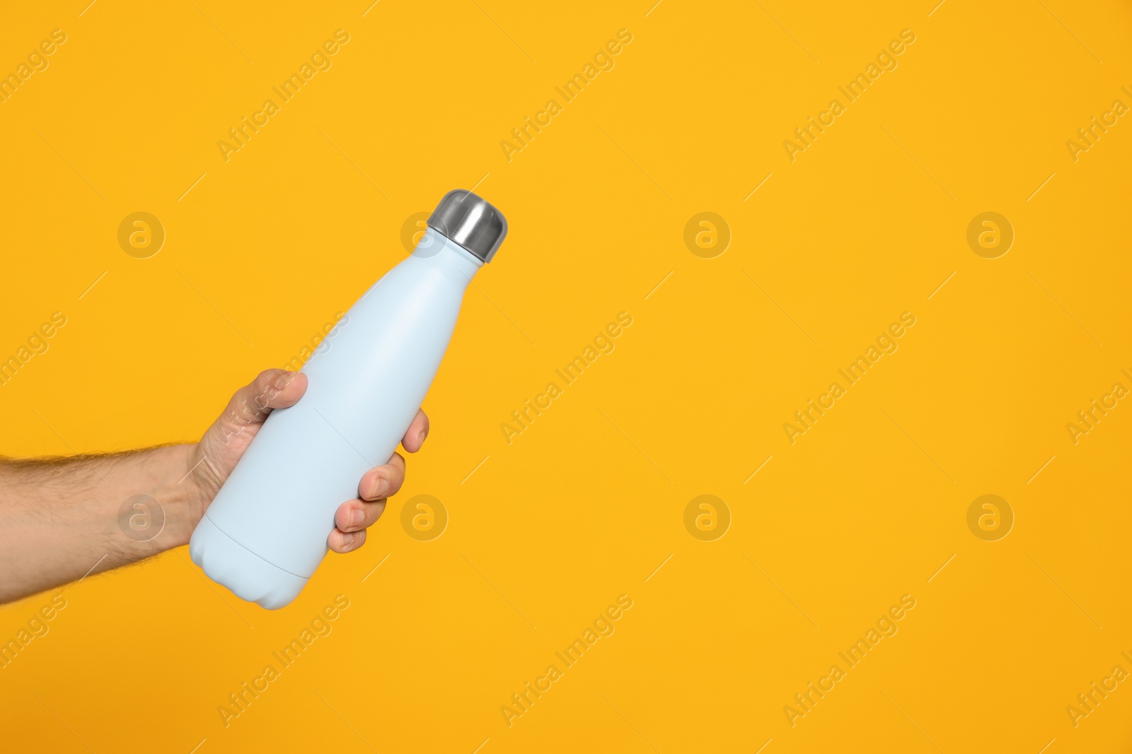 Photo of Man holding thermo bottle on orange background, closeup. Space for text