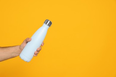 Man holding thermo bottle on orange background, closeup. Space for text