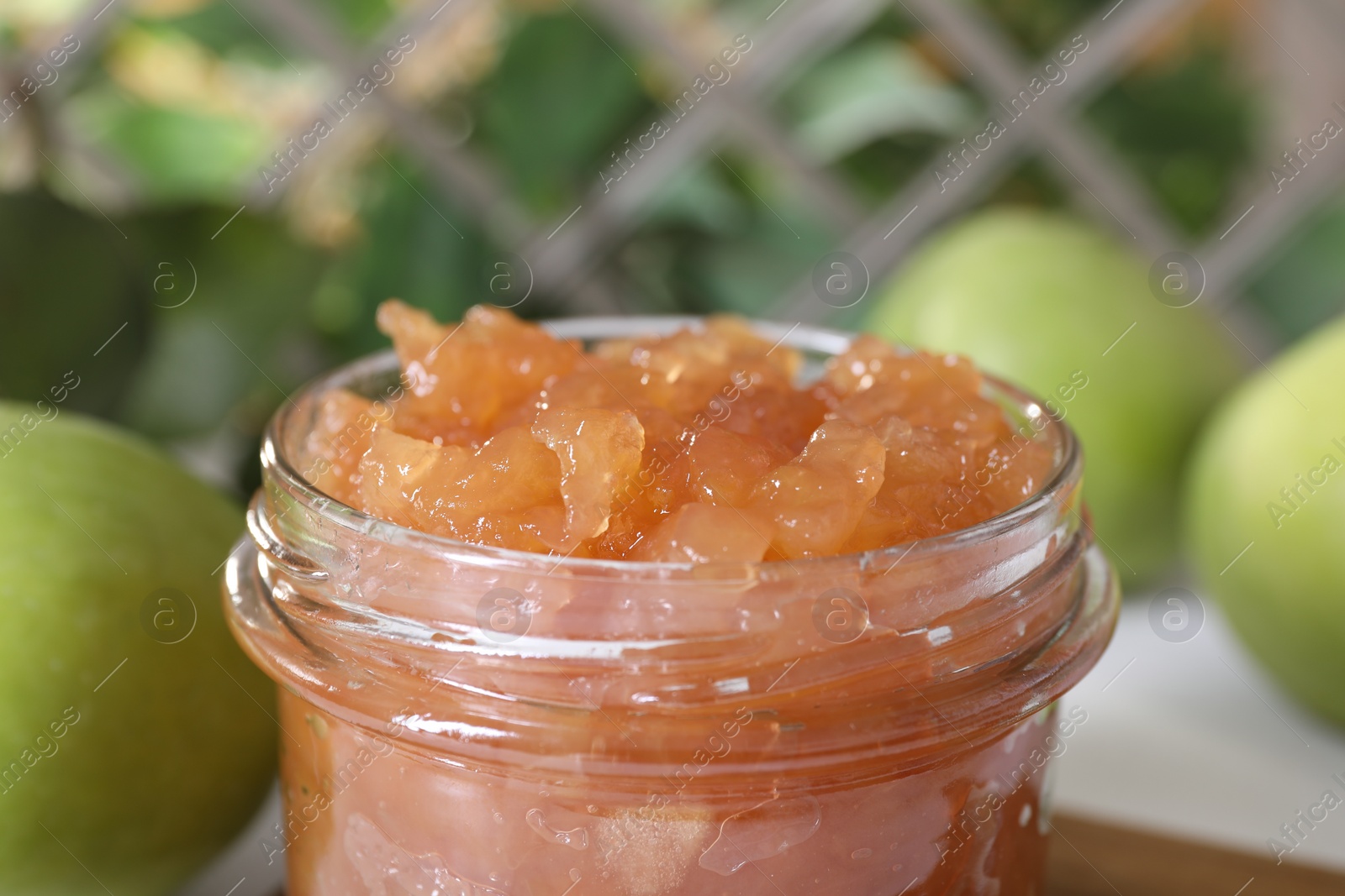 Photo of Glass jar of delicious apple jam against blurred background, closeup