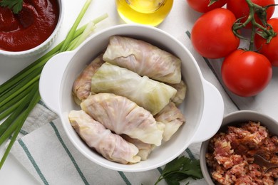 Uncooked stuffed cabbage rolls and ingredients on table, flat lay