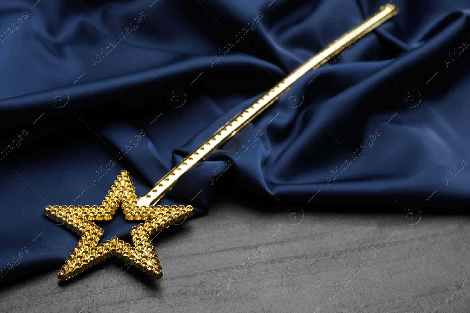 Photo of Beautiful golden magic wand and blue fabric on black table