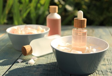 Photo of Bottles of rose essential oil and petals on light blue wooden table, closeup