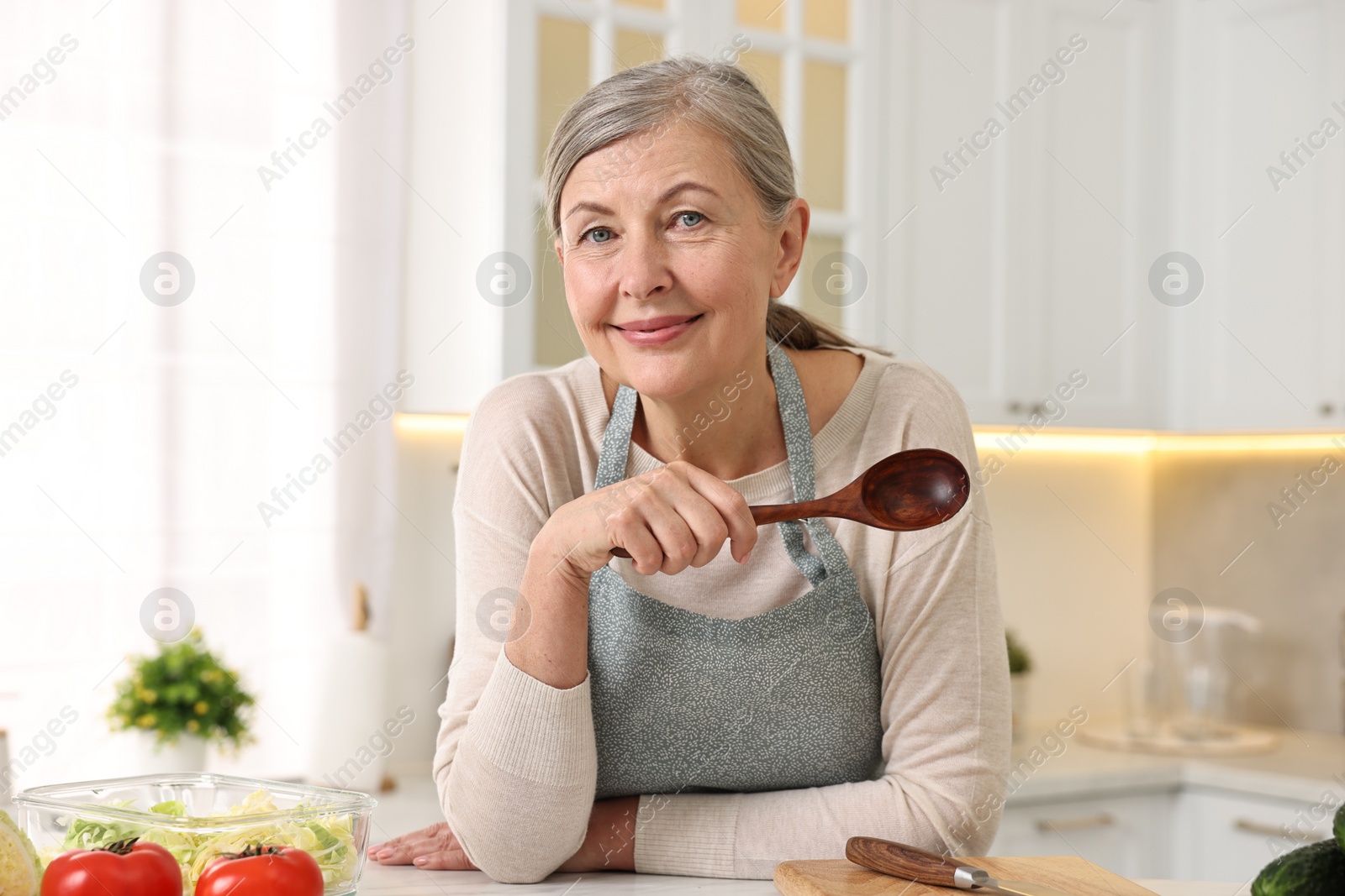 Photo of Happy housewife with spoon at table in kitchen