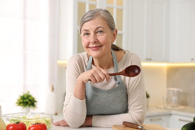 Photo of Happy housewife with spoon at table in kitchen