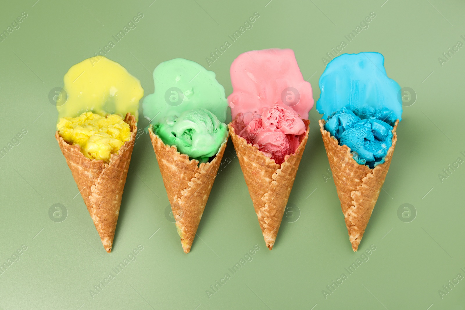 Photo of Melted ice cream in wafer cones on pale green background, flat lay