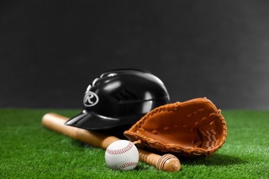 Photo of Baseball bat, batting helmet, leather glove and ball on green grass against dark background