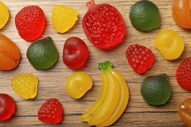 Photo of Delicious gummy fruit shaped candies on wooden table, flat lay