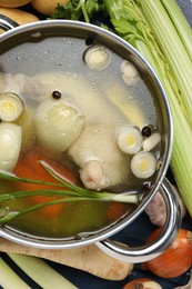 Pot with tasty bouillon and different ingredients on blue wooden table, flat lay