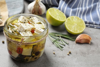 Composition with pickled feta cheese in jar on grey table, space for text