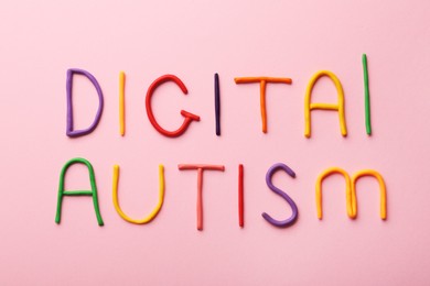 Photo of Phrase Digital Autism made of colorful plasticine on pink background, flat lay. Addictive behavior