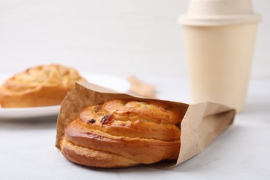 Delicious roll with raisins in paper bag on white table, closeup. Sweet bun