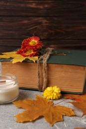 Photo of Book decorated with chrysanthemum flowers, autumn leaves and scented candle on light gray textured table