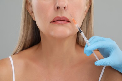 Photo of Doctor giving facial injection to senior woman on light grey background, closeup. Cosmetic surgery