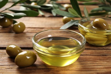 Bowls with cooking oil and olives on wooden table, closeup