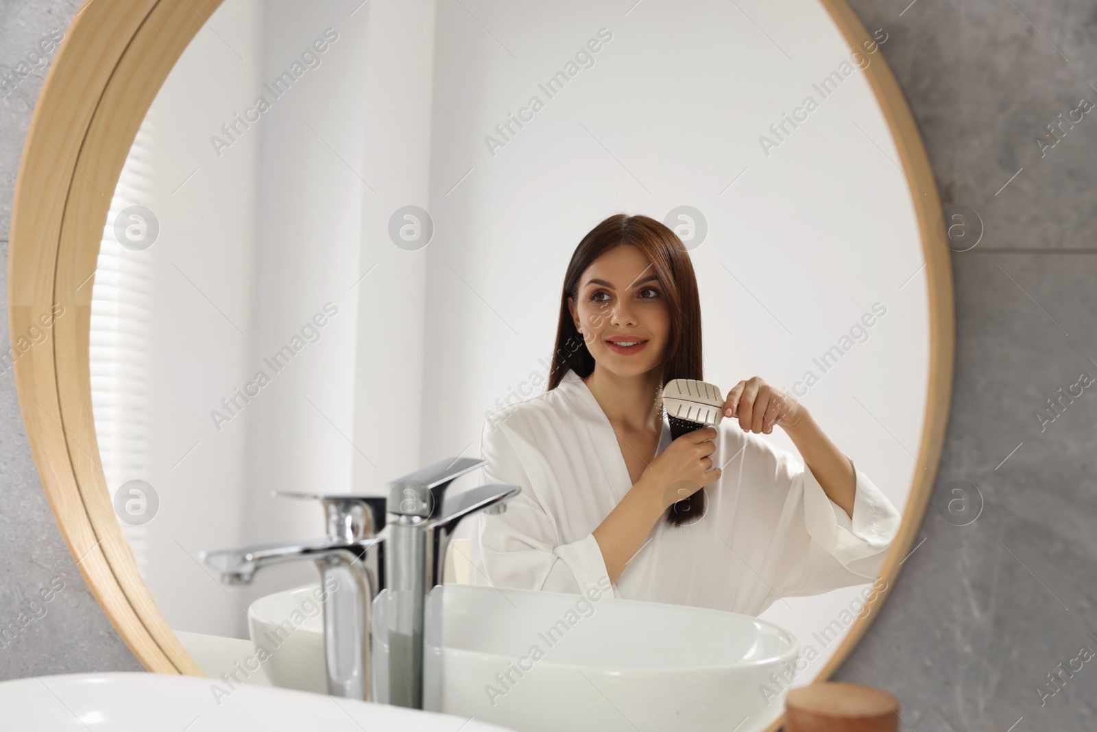 Photo of Beautiful woman brushing her hair near mirror in bathroom