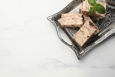 Photo of Tasty chocolate halva and mint on white marble table, top view. Space for text