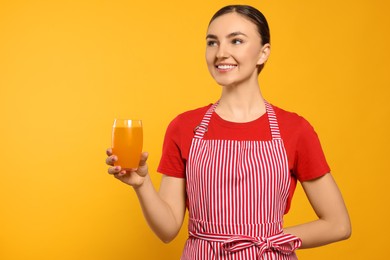 Photo of Beautiful young woman in clean striped apron with glass of juice on orange background