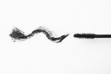 Photo of Applicator and black mascara smear for eyelashes on white background, top view