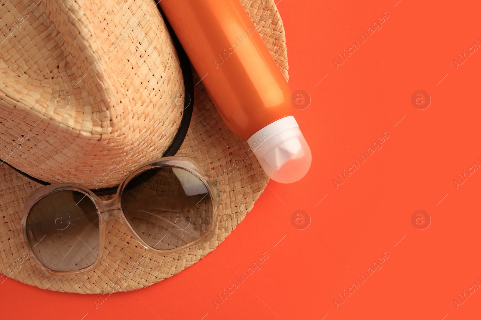Photo of Bottle of sunscreen and beach accessories on coral background, top view. Space for text