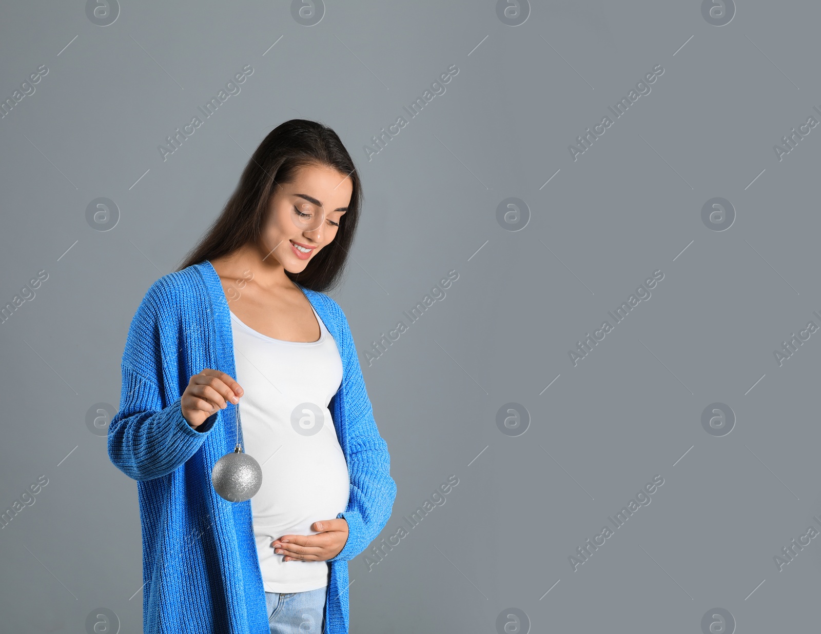 Photo of Happy pregnant woman with Christmas ball on grey background, space for text. Expecting baby