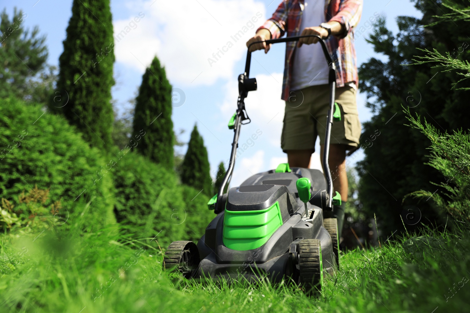 Photo of Man cutting grass with lawn mower in garden on sunny day, closeup