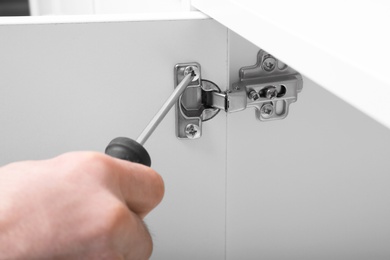 Photo of Man fixing door of white wardrobe with screwdriver, closeup