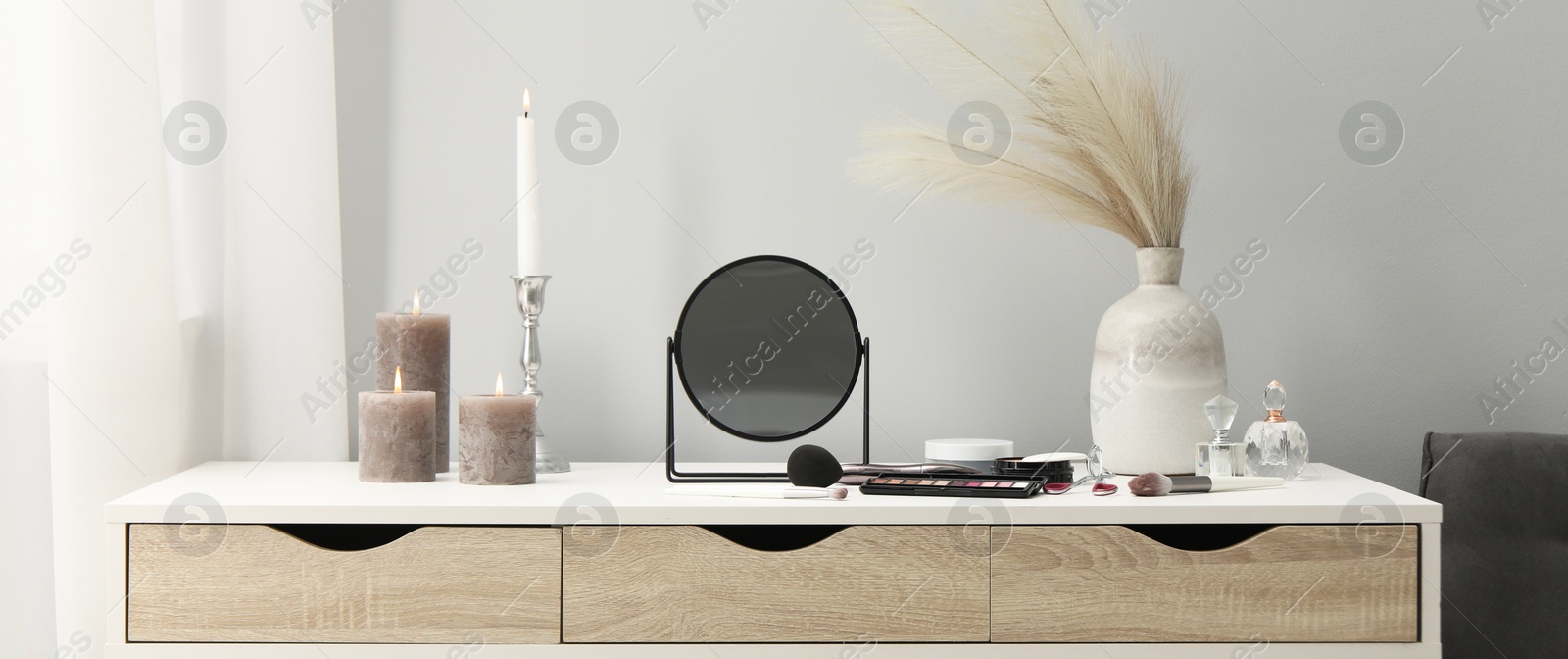 Image of Makeup room. Mirror, cosmetic products, perfumes and burning candles on dressing table indoors, banner design