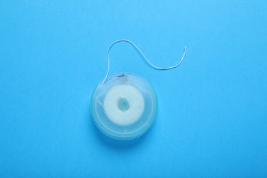 Container with dental floss on light blue background, top view