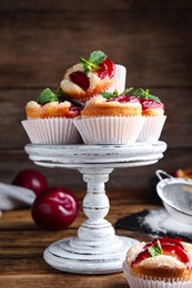 Photo of Delicious sweet cupcakes with plums on wooden table