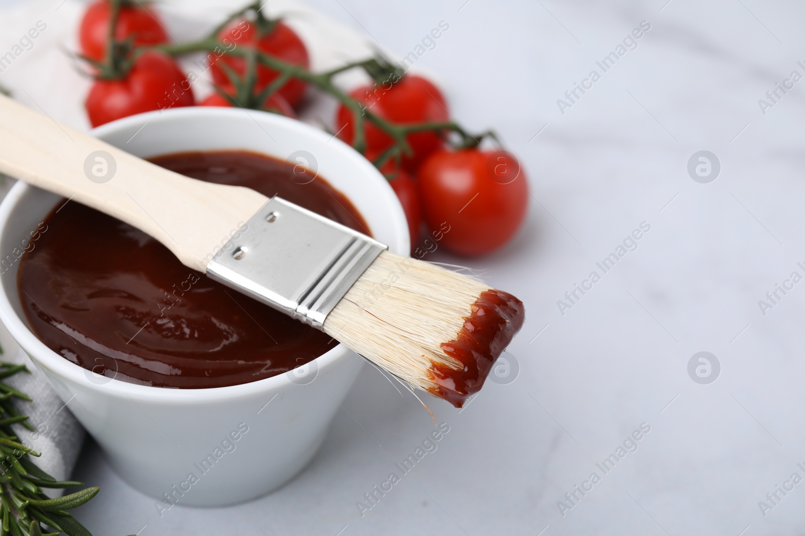 Photo of Marinade in bowl and basting brush on white marble table, closeup. Space for text