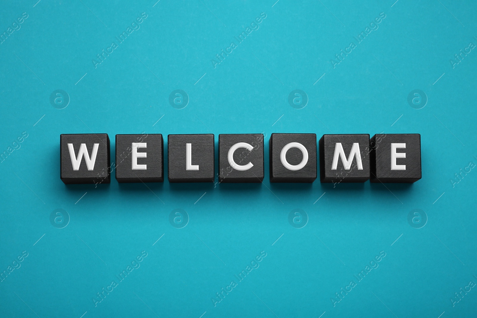 Photo of Word Welcome made of black cubes with letters on turquoise background, top view
