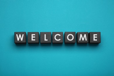 Photo of Word Welcome made of black cubes with letters on turquoise background, top view