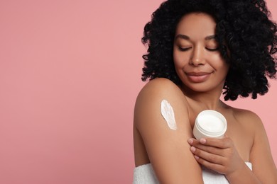 Young woman applying body cream onto shoulder on pink background. Space for text