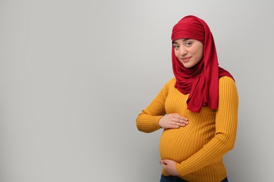 Portrait of pregnant Muslim woman in hijab on light gray background, space for text