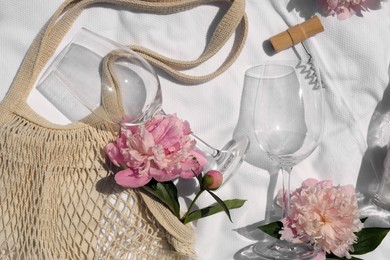 Flat lay composition with beautiful peonies and wineglasses on white fabric
