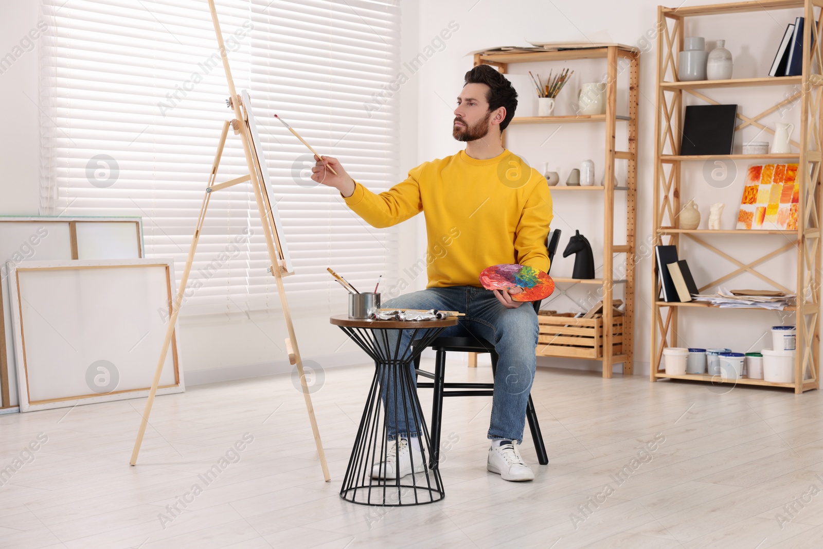 Photo of Man painting in studio. Using easel to hold canvas