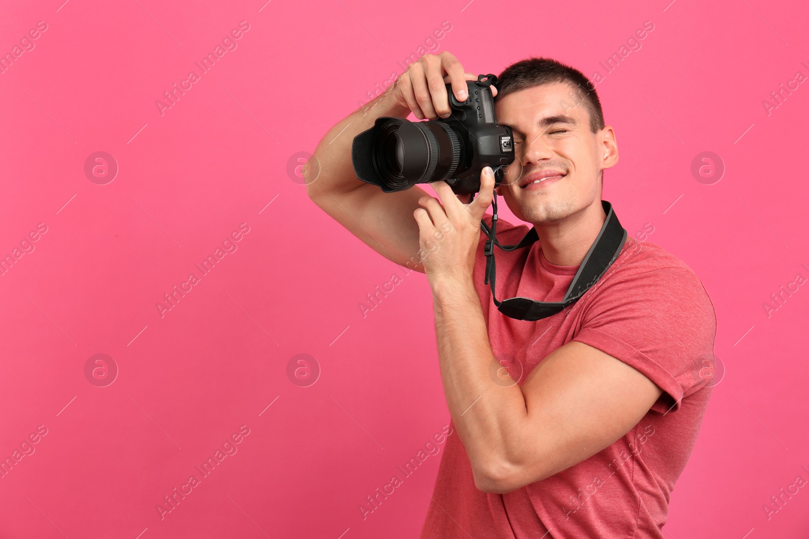 Photo of Young professional photographer taking picture on pink background. Space for text