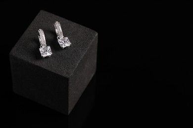 Stylish presentation of elegant earrings on black podium, space for text. Luxury jewelry