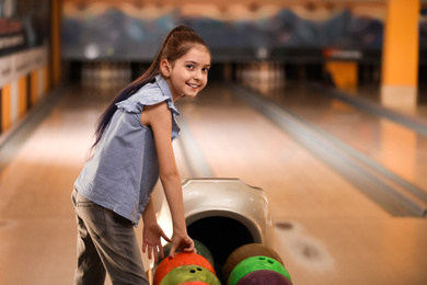 Photo of Little girl near balls in bowling club. Space for text