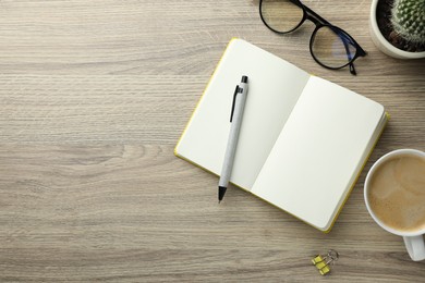 Open notebook, pen, glasses and cup of coffee on wooden table, flat lay. Space for text